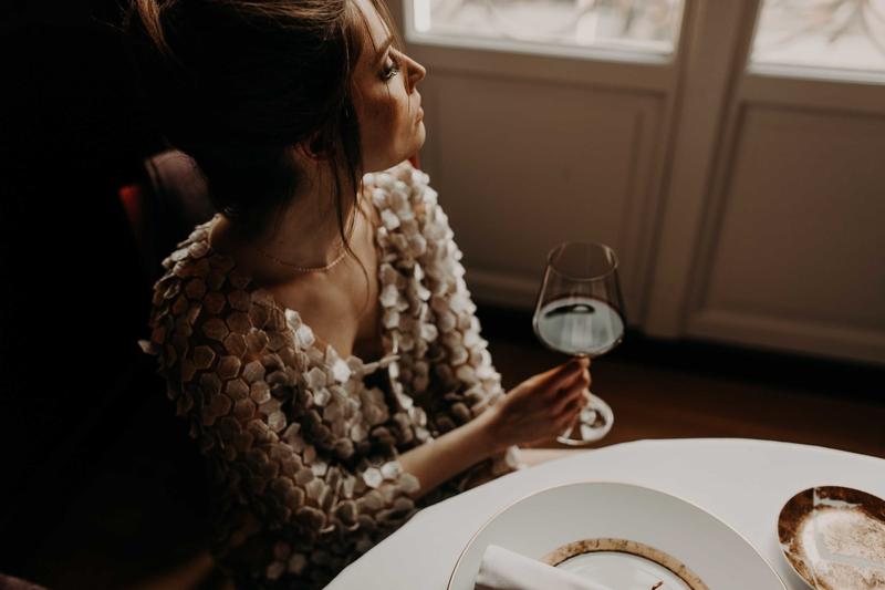 Girl set at restaurant table at Le Pressoir d'Argent holding glass of red wine looking out of window