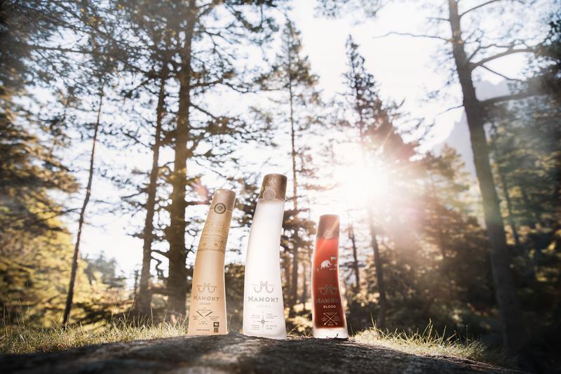 Full range of Mamont vodka bottles sat on rock with sunlight shining through trees