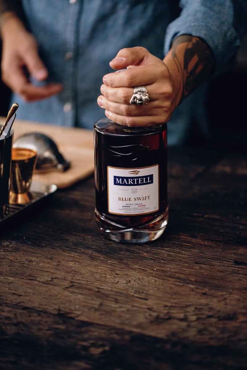 Close up of hand placing bottle of Martell Blue Swift onto a table