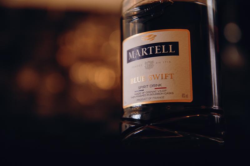 Close up of bottle of Martell Blue swift sat on bar with lights in background