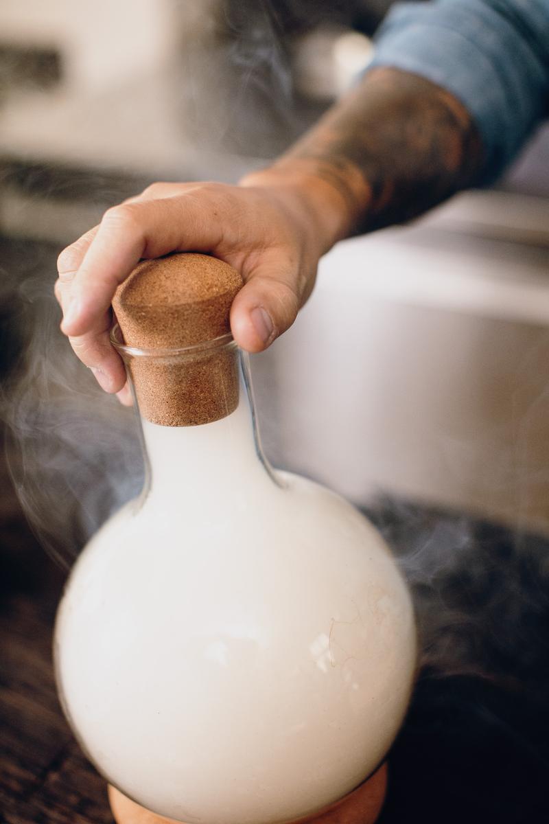 Close up of hand putting bung on flask used to smoke a cocktail